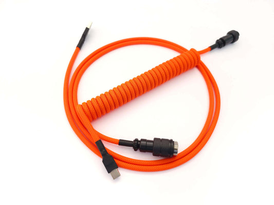 Coiled cable designed for GMK CYL Flare keycaps. In neon orange color, with black Aviator Gx16 connector and black heat-shrink. USB C to A connection.